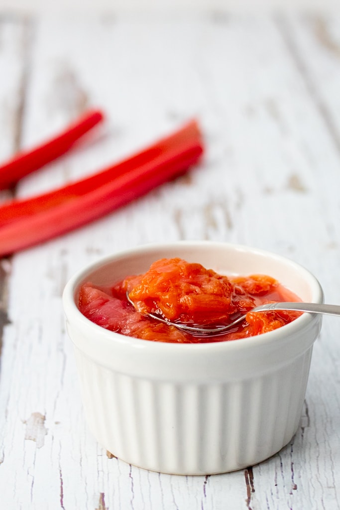 bowl of stewed rhubarb with rhubarb stalks in the background