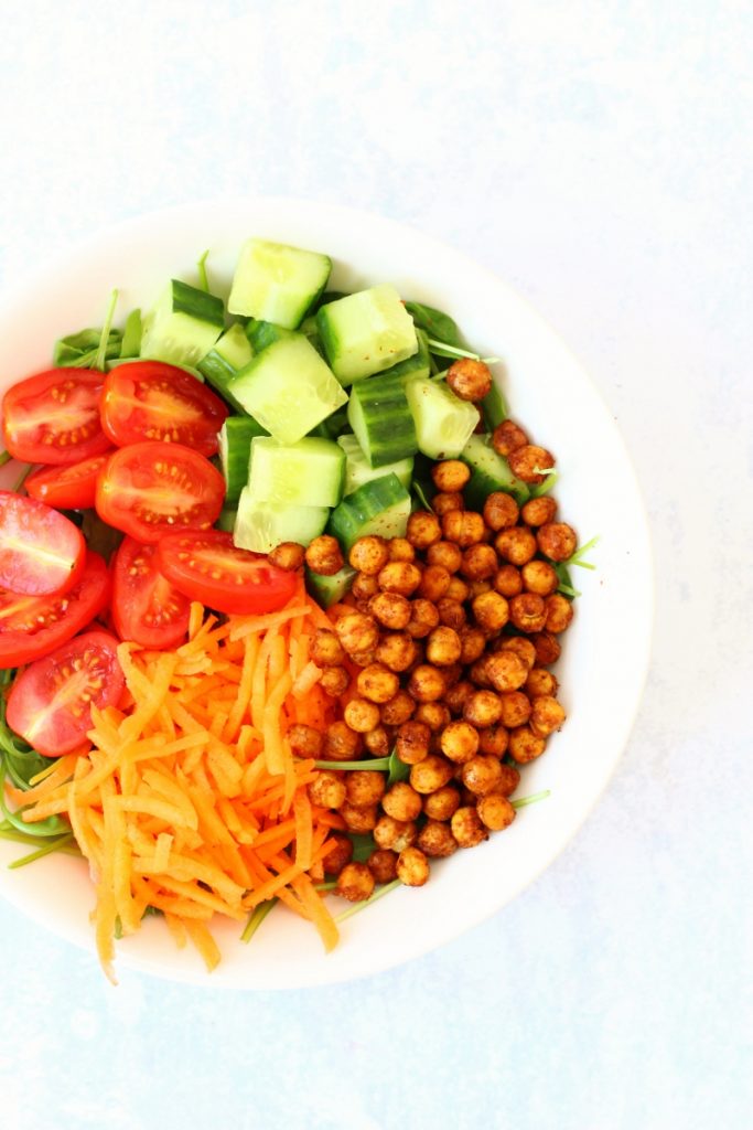 Bowl of salad including roasted chickpeas, cucumber, tomatoes and grated carrot