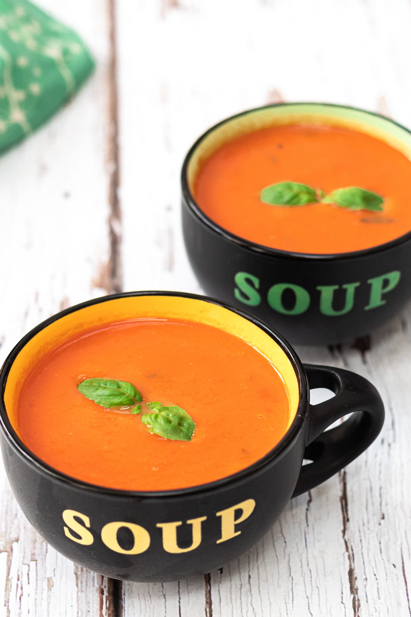 two bowls of tomato soup with basil on top