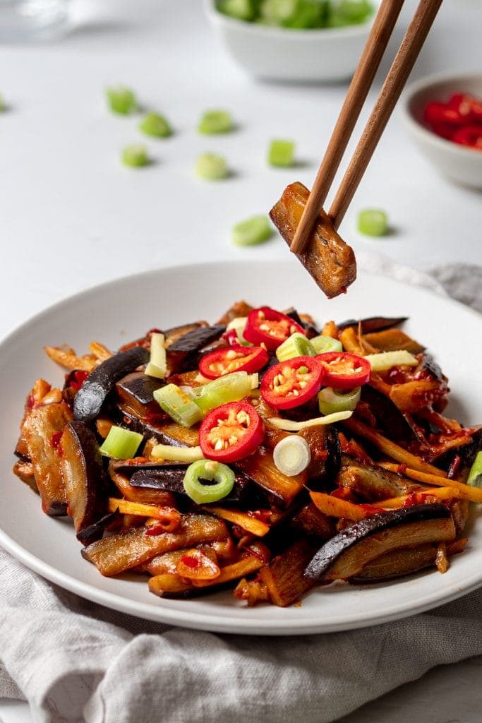 chopsticks holding a piece of aubergine in chilli bean paste