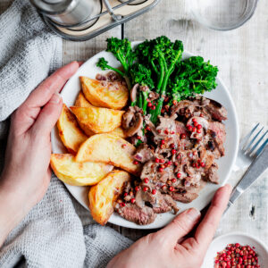 Plate of steak with potato wedges, broccoli and pink peppercorn sauce
