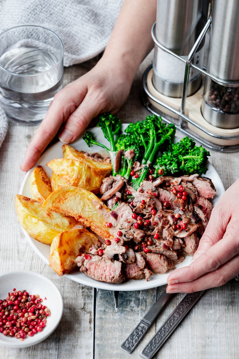 Habds putting down a plate of steak with pink peppercorn sauce
