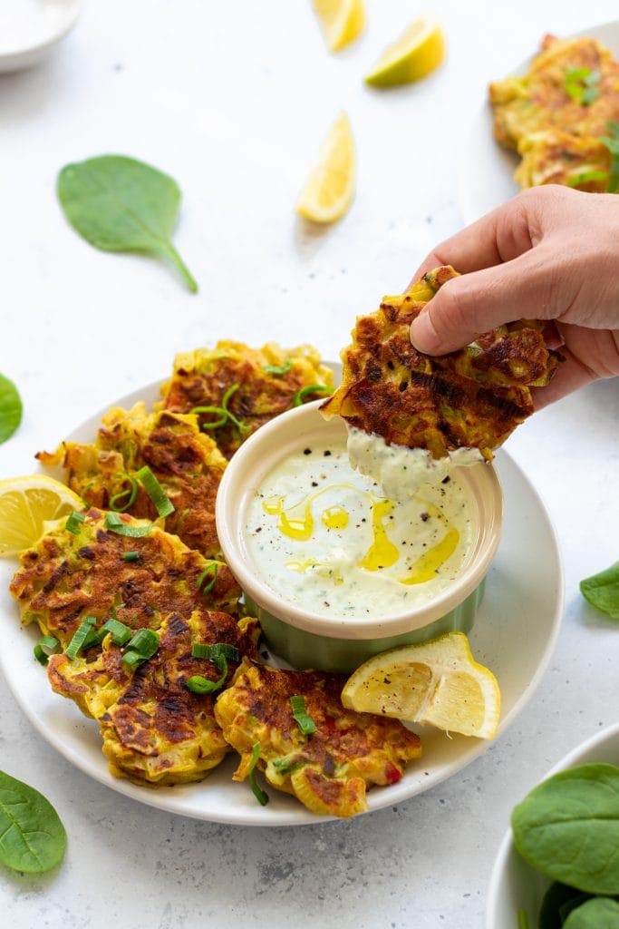 hand dipping a leek fritter in garlic sauce