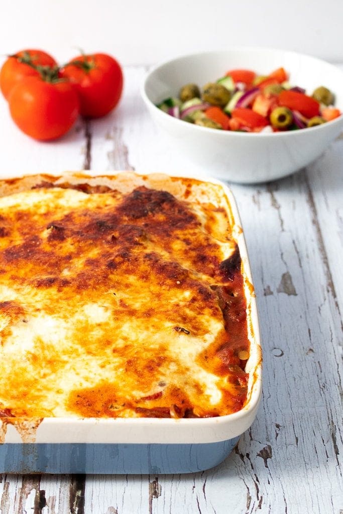 Dish of vegetarian Moussaka with salad and tomatoes in the background