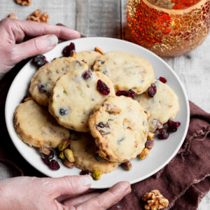Hands holding a plate of nut and cranberry biscuits