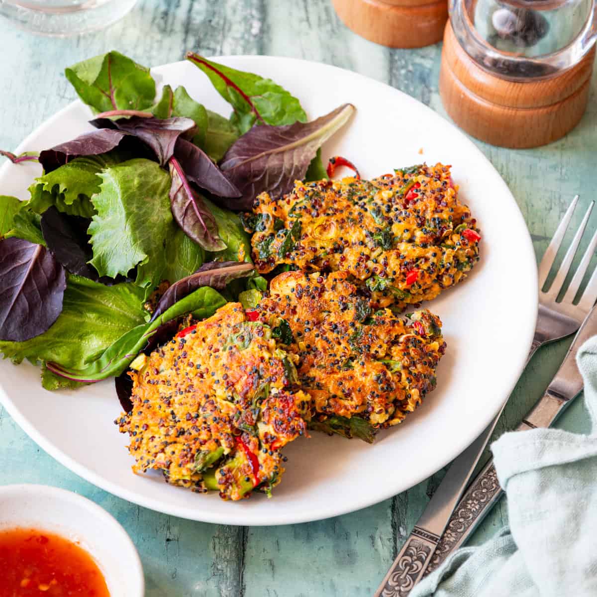 Three quinoa patties on a plate with salad leaves