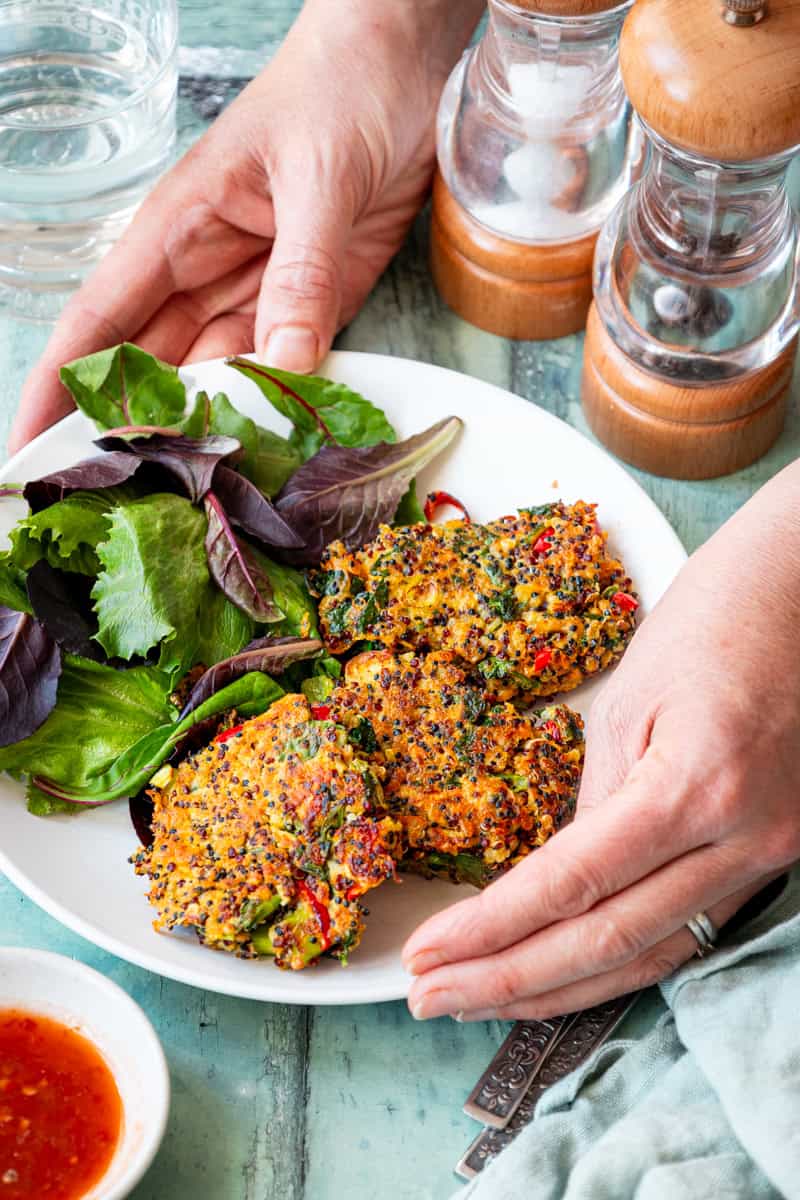 Hands holding a plate of crispy vegetarian quinoa patties