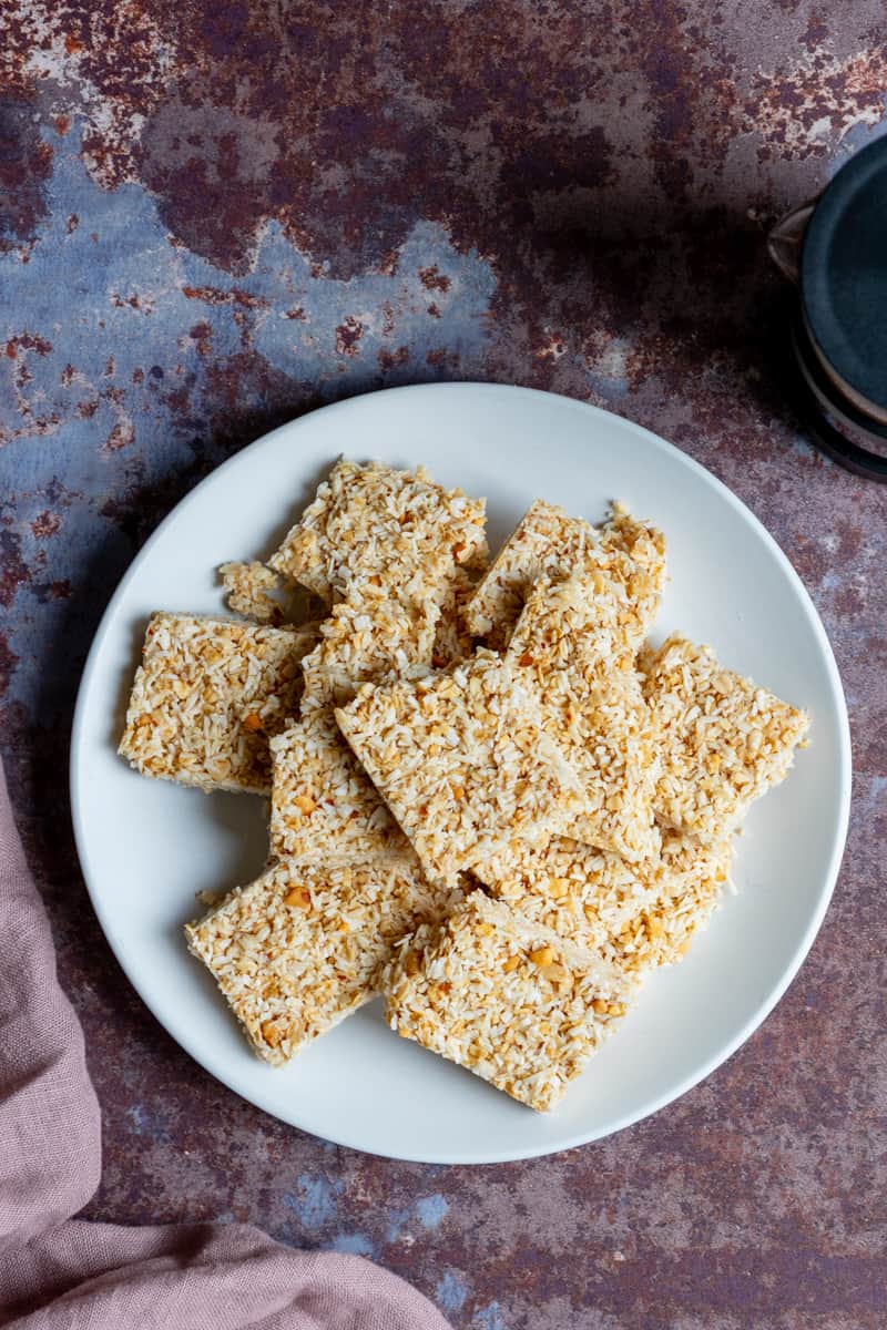 Plate of no bake peanut butter coconut bars next to pot of coffee
