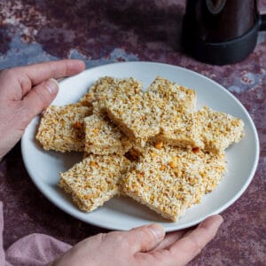 Hands holding plate of coconut peanut butter bars