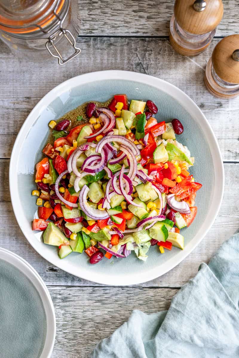 Plate of Mexican kilner jar salad with onions, avocado, kidney beans, tomatoes, bell peppers