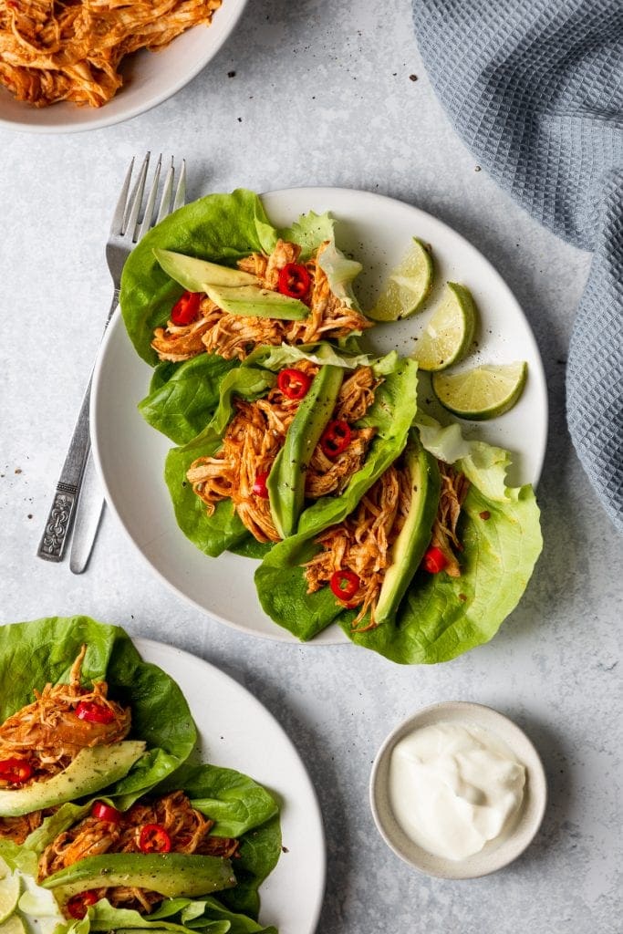 two plates of shredded sriracha chicken lettuce tacos