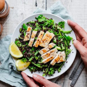 Hands holding a plate of black quinoa and chicken salad