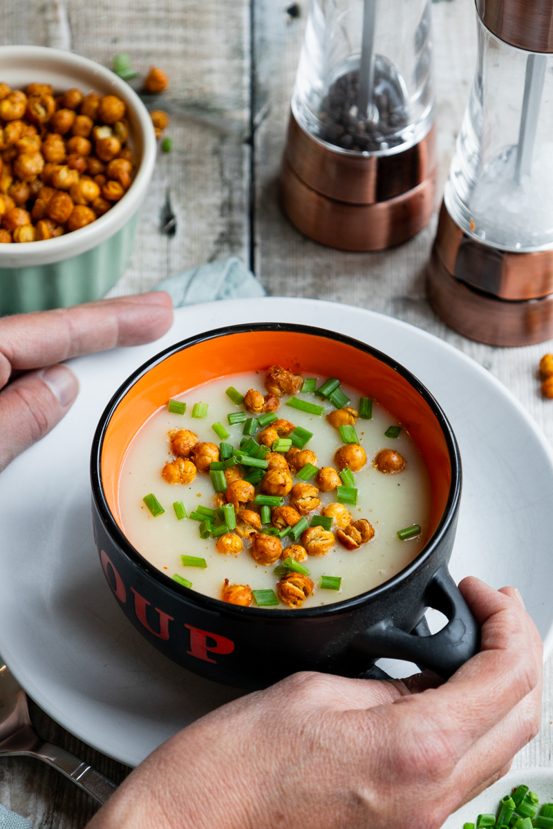 hands holding a bowl of roasted garlic and potato soup