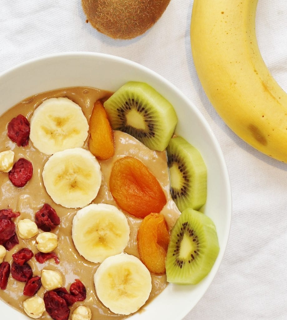 Healthy Nutella smoothie bowl with banana and avocado topped with banana, kiwi fruit, dried apricots, cranberries and hazelnuts