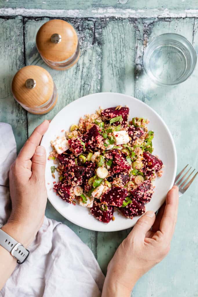 Hands holding a plate of couscous beetroot feta salad