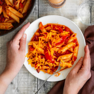 hands holding bowl of spicy tomato pasta