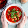 Bowl of tomato and sausage soup with hands
