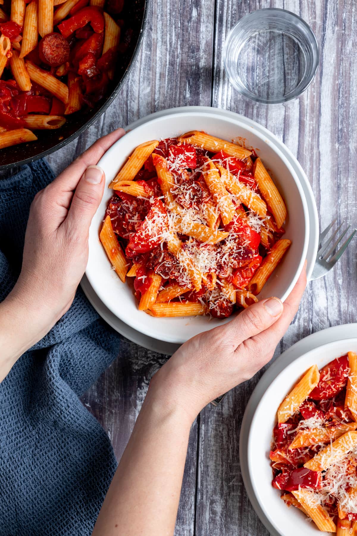 Hands holding bowl of tomato and chorizo pasta
