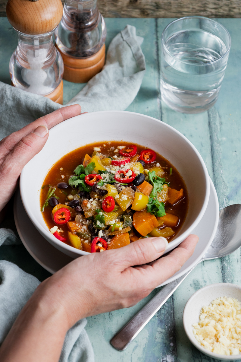 Hands holding bowl of black bean and sweet potato soup
