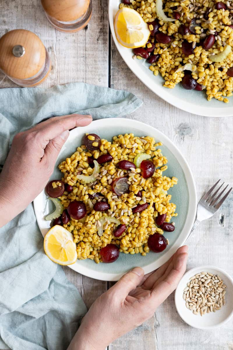 Hands holding a plate of pearl barley salad