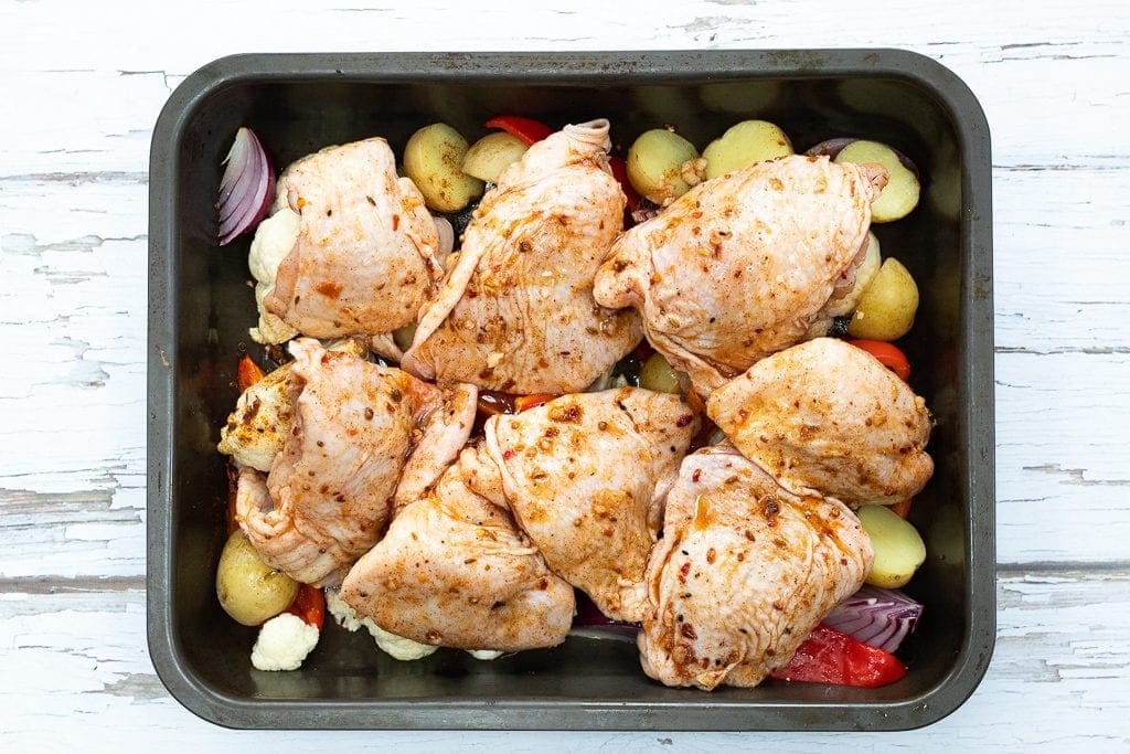 chicken thighs ready for the oven on top of roasted vegetables