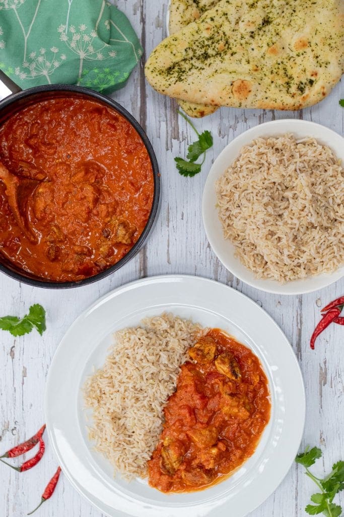 flatlay of chicken tikka masala on a plate with a bowl of rice, naan breads and a pot of the curry