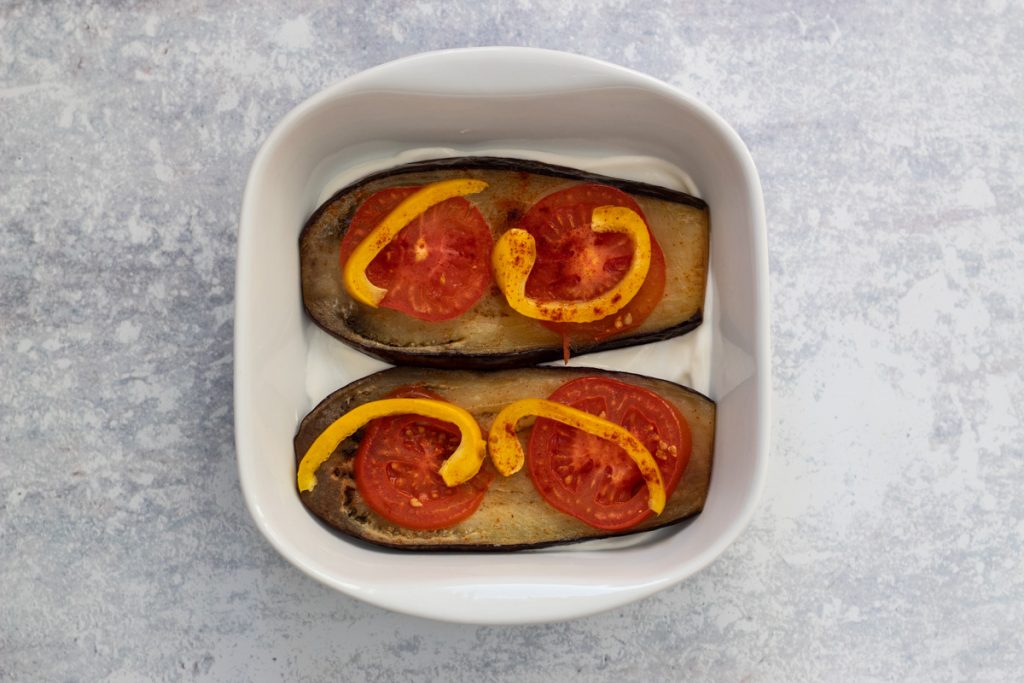 Assembling layers of aubergine, tomatoes, peppers and yogurt in a serving dish