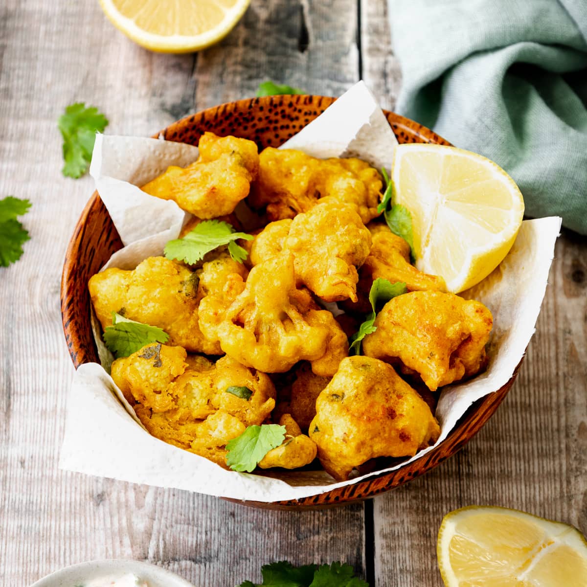 Cauliflower pakoras in a bowl with lemon wedges on teh side
