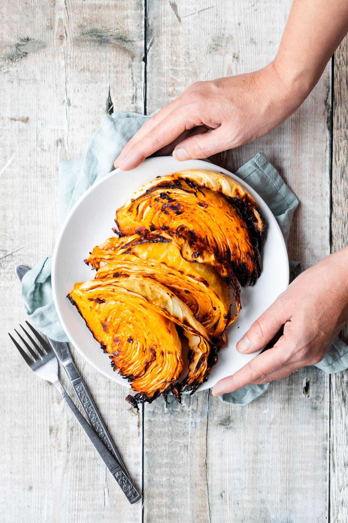 Hands holding a plate of harissa air fried cabbage wedges