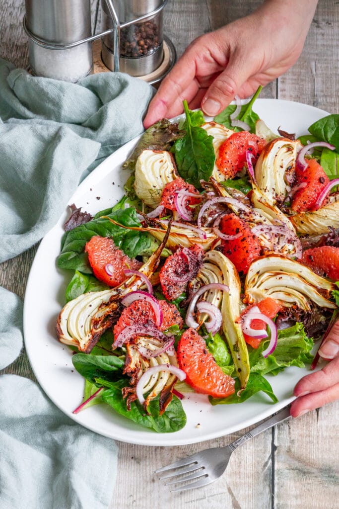 hands putting down a plate of fennel and grapefruit salad