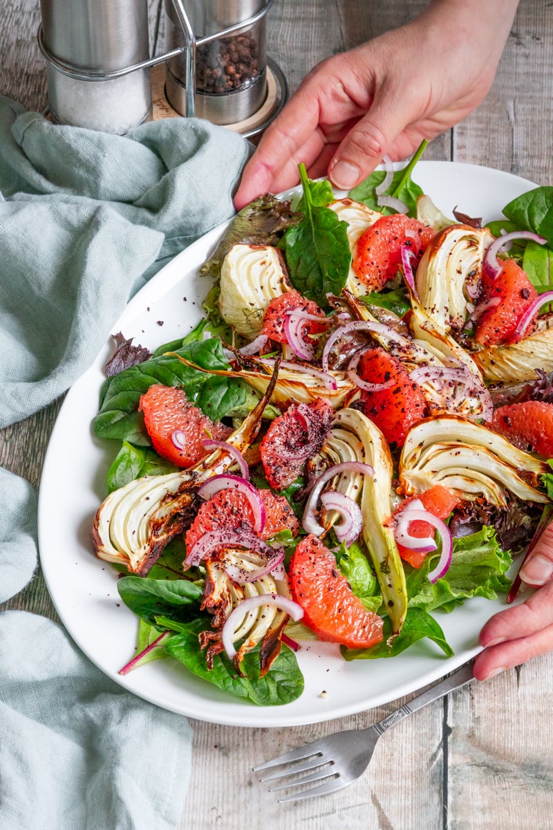 hands putting down a plate of fennel and grapefruit salad
