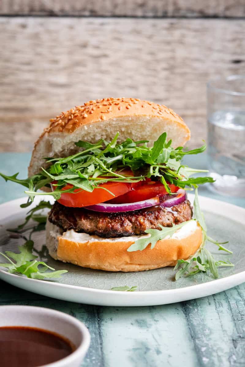 lamb burger in a bun next to a bowl of bbq sauce