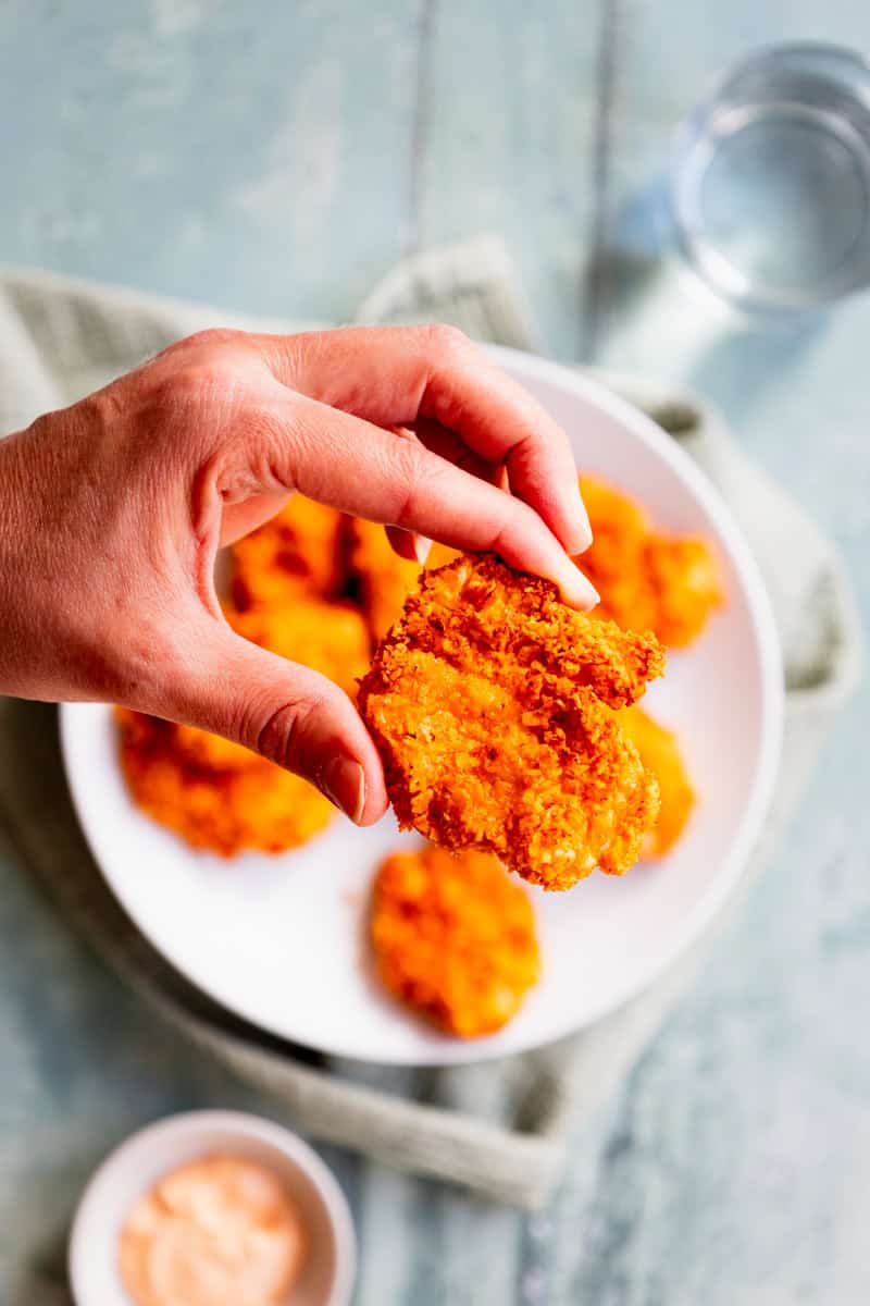 Hand holding a piece of Doritos coated chicken