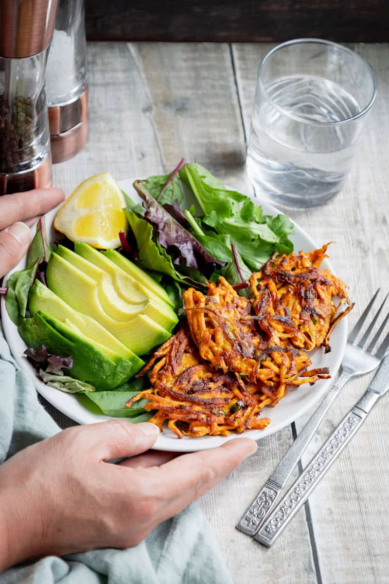 Hands holding a plate of sweet potato fritters