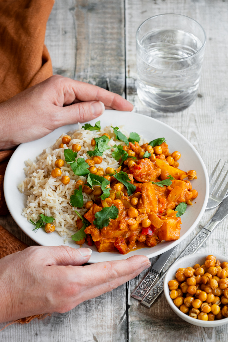 Hands holding plate of potato and chickpea curry