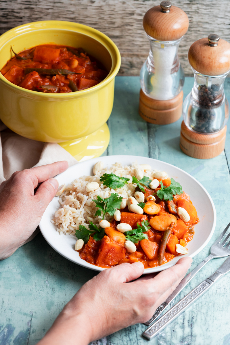 Hands putting down a plate of African peanut stew with butter beans