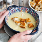 Bowl of chicken and ginger soup with hands